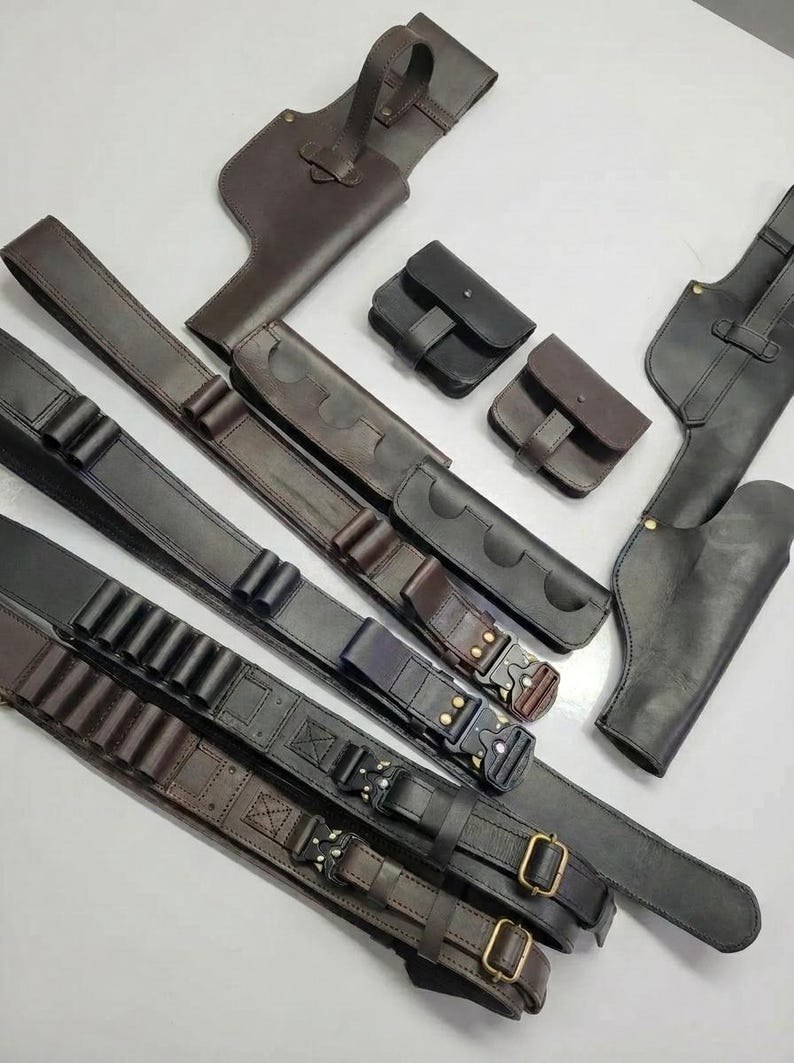 K&ouml;nnte beinhalten: Eine Auswahl handgefertigter Lederholster, G&uuml;rtel und Taschen in verschiedenen Braun- und Schwarzt&ouml;nen. Das Bild zeigt verschiedene Designs, darunter Waffenholster, Patroneng&uuml;rtel und kleine Taschen mit Schnallen- und Riemenverschl&uuml;ssen.