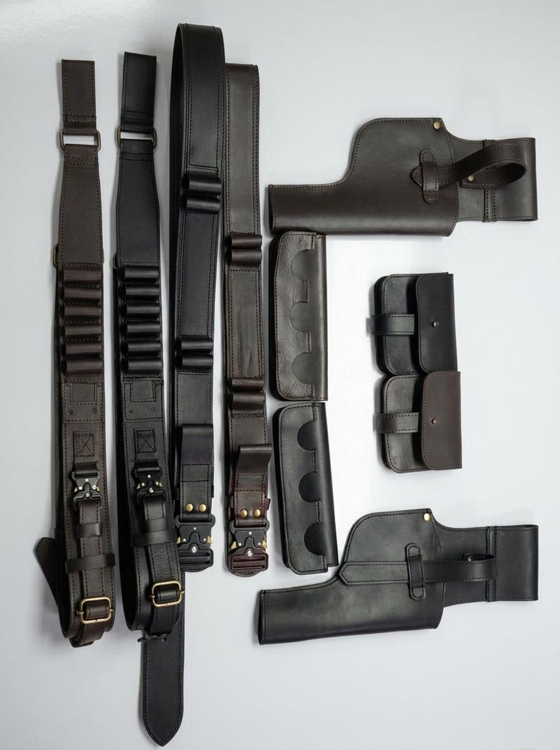 K&ouml;nnte beinhalten: Eine Auswahl an dunkelbraunen und schwarzen Leder-Waffenzubeh&ouml;r, darunter Riemen, Patronenhalter und Holster. Die Artikel sind auf einer wei&szlig;en Oberfl&auml;che angeordnet und zeigen die verschiedenen Designs und Hardware-Details.
