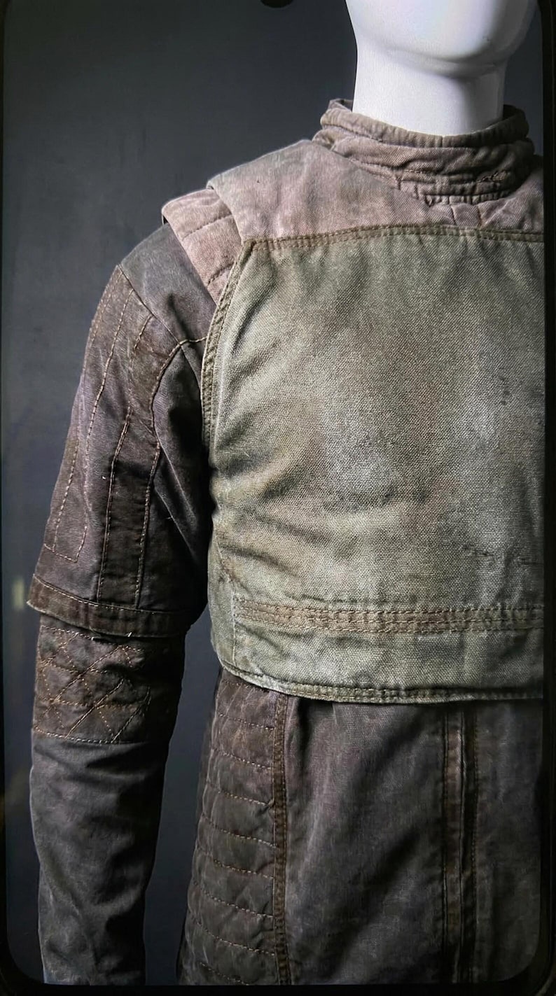 Puede incluir: Chaqueta desgastada en verde oliva y marr&oacute;n con detalles acolchados. La chaqueta tiene cuello alto y hombros acolchados. Las mangas tienen un dise&ntilde;o en capas. La prenda se exhibe en un maniqu&iacute;.