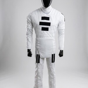 May include: White jumpsuit with black accents, displayed on a mannequin. The outfit features a high collar, quilted detailing, and black rectangular patches on the chest and legs. The mannequin has a black head and hands, and the outfit appears to be a costume.