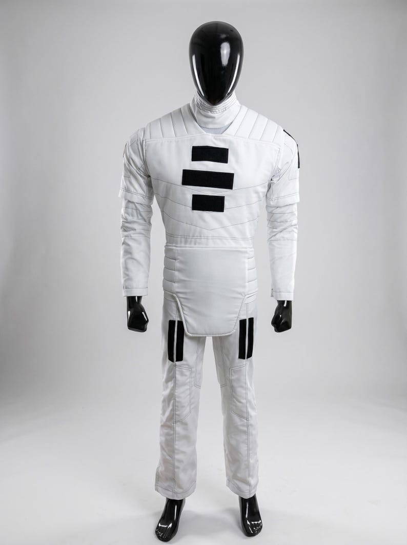 May include: White jumpsuit with black accents, displayed on a mannequin. The outfit features a high collar, quilted detailing, and black rectangular patches on the chest and legs. The mannequin has a black head and hands, and the outfit appears to be a costume.