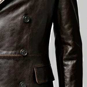 K&ouml;nnte beinhalten: Dunkelbraune Lederjacke mit doppelreihigem Design. Die Jacke hat drei sichtbare Kn&ouml;pfe, ein fallendes Revers und eine kleine Tasche. Das Leder hat ein Used-Look-Aussehen.