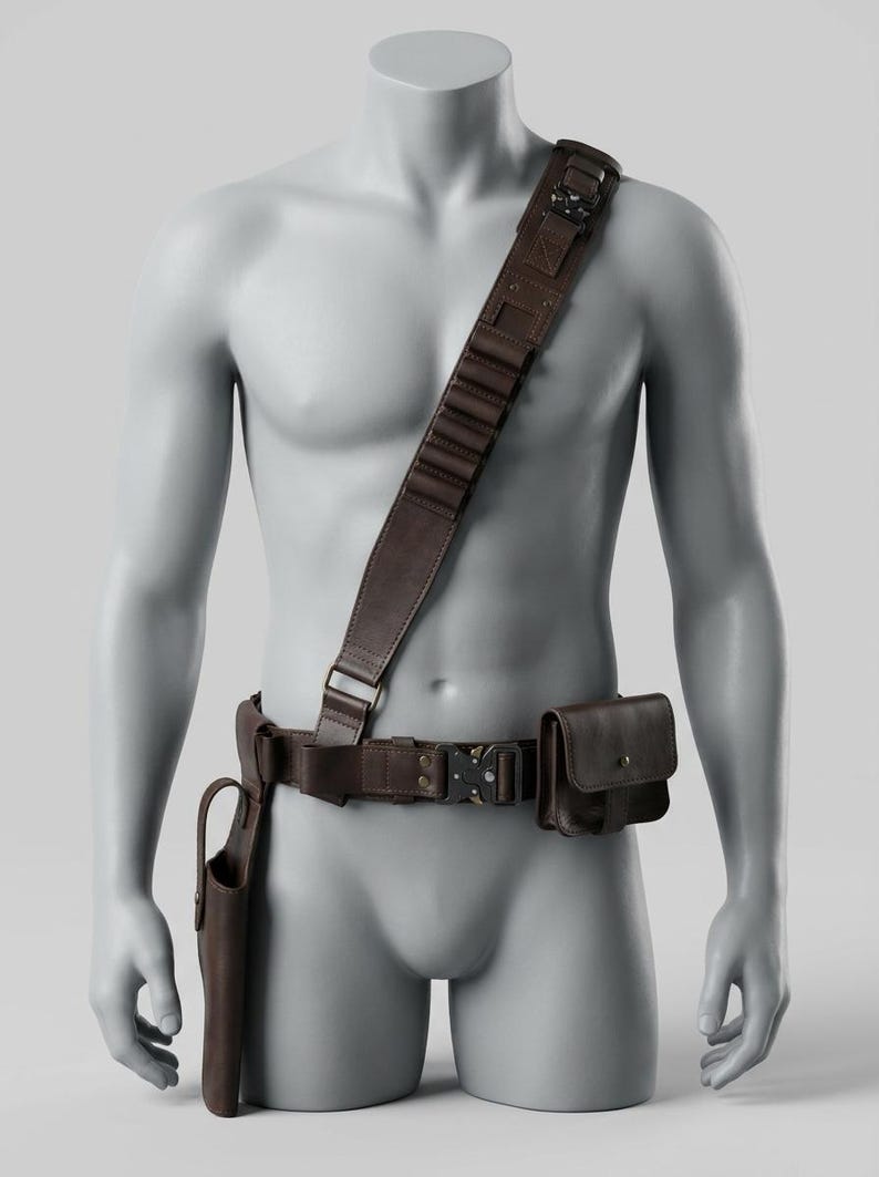 K&ouml;nnte beinhalten: Brauner Leder-Utility-G&uuml;rtel mit Schulterriemen, Holster und Tasche. Der G&uuml;rtel hat eine Metallschnalle und ist f&uuml;r das Tragen &uuml;ber der Brust konzipiert. Das Holster befindet sich auf der linken Seite und die Tasche auf der rechten Seite.