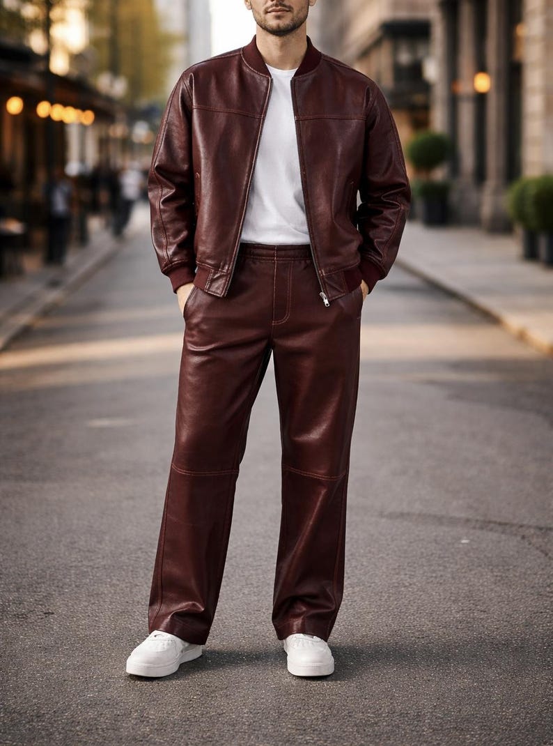 May include: A burgundy leather bomber jacket and matching pants are worn with a white t-shirt and white sneakers. The jacket has a zip closure and ribbed cuffs. The pants are straight-legged.