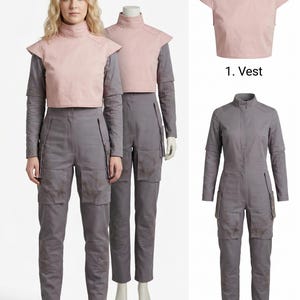 Op de afbeelding: Een vrouw en een mannequin dragen een tweedelige outfit en een jumpsuit. De tweedelige outfit bestaat uit een roze vest en een grijs shirt met lange mouwen en een broek. De jumpsuit is grijs met meerdere zakken. De outfit is waarschijnlijk een kostuum.