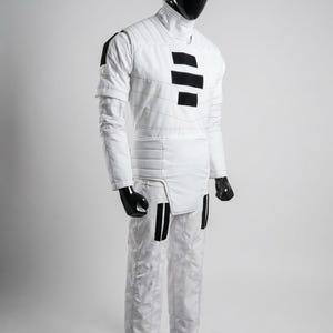 May include: White quilted jumpsuit with black accents. The costume features a high collar, long sleeves, and black rectangular details on the chest and legs. The mannequin's head and hands are black.