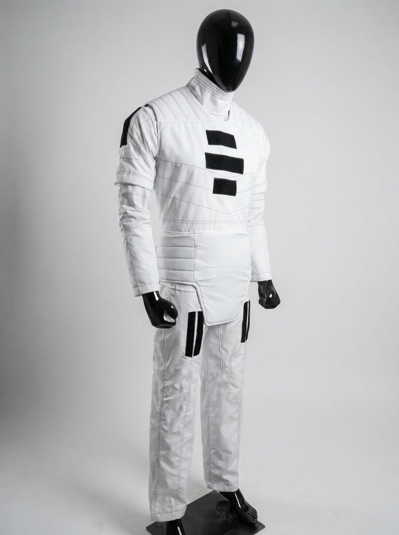 May include: White quilted jumpsuit with black accents. The costume features a high collar, long sleeves, and black rectangular details on the chest and legs. The mannequin's head and hands are black.