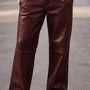 May include: A pair of burgundy leather pants with a straight leg design. The pants have visible stitching and a smooth, shiny texture. The model is wearing a matching burgundy leather jacket.