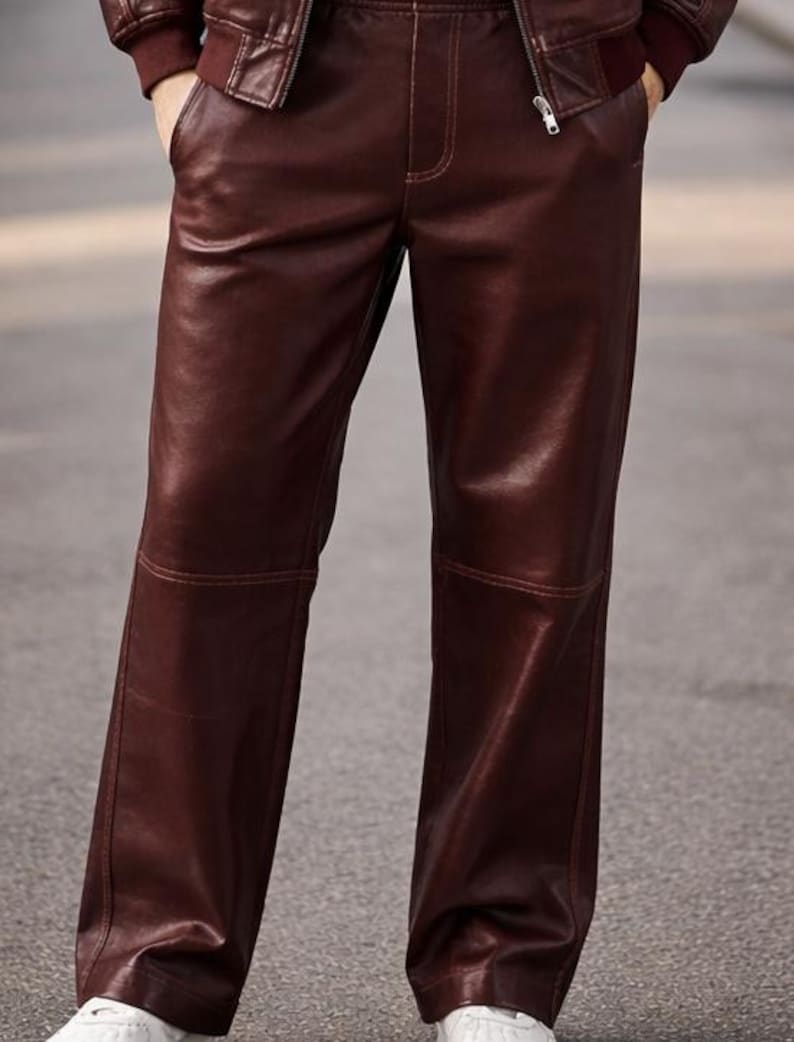 May include: A pair of burgundy leather pants with a straight leg design. The pants have visible stitching and a smooth, shiny texture. The model is wearing a matching burgundy leather jacket.