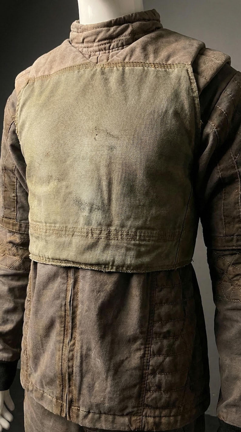 Puede incluir: Chaqueta marr&oacute;n y verde oliva con dise&ntilde;o acolchado en mangas y hombros. La chaqueta tiene un aspecto en capas con un panel verde claro en el pecho. La tela parece desgastada y texturizada.