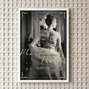 May include: A framed movie poster in black and white, featuring a woman in an elegant gown with the title "Phantom Thread" in gold script. The poster includes the names of the actors and director.