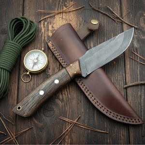 May include: A survival kit featuring a fixed-blade knife with a wooden handle and leather sheath, a brass compass, and a coil of green rope. The items are arranged on a dark wooden surface with pine needles.