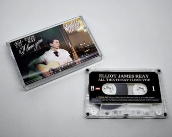 May include: A clear cassette tape and case featuring the album "All This to Say I Love You" by Elliot James Reay. The album art shows a man playing a guitar. The cassette tape has a black label with white text.