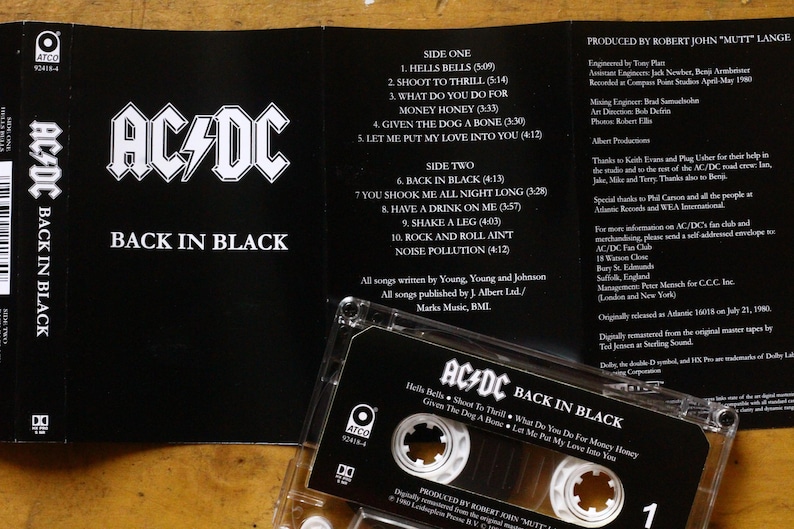 May include: AC/DC's "Back in Black" album on cassette tape. The black cassette case is open, revealing the tracklist and album art. The album title and band logo are prominently displayed.