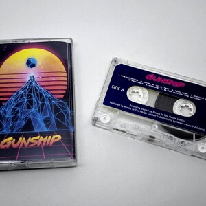 Può includere: Una musicassetta trasparente con un design retrò raffigurante una montagna, una forma geometrica e un tramonto. La custodia della cassetta è accanto alla cassetta. Il testo "GUNSHIP" è visibile sulla custodia e sull'etichetta della cassetta.
