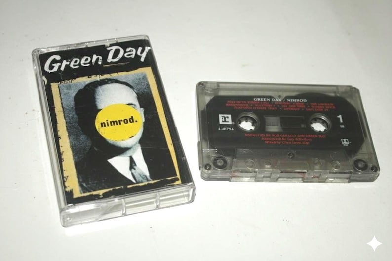 May include: A Green Day "Nimrod" cassette tape and case. The case features the band's name and album title, along with a black and white image of a man with a yellow circle over his face. The cassette tape is black with white text.