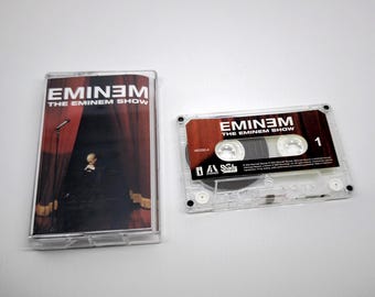 Könnte beinhalten: Eine transparente Kassette und Hülle mit dem Albumcover von Eminems "The Eminem Show". Das Albumcover zeigt eine Bühne mit roten Vorhängen und eine Person auf der Bühne. Die Kassette ist mit "1" beschriftet.