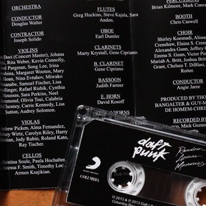 May include: A black cassette tape with the Daft Punk logo and album title "Random Access Memories" is displayed. The cassette is in a clear plastic case, with the album credits in the background.