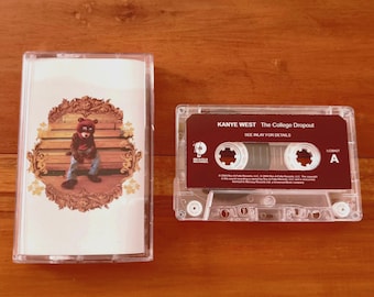May include: Two cassette tapes on a wooden surface. One tape has a cover featuring a bear wearing a graduation cap sitting on a bench. The other tape is transparent with a maroon label that reads "Kanye West The College Dropout".