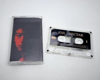 May include: A clear plastic cassette case with a Joji Nectar album cover insert featuring a portrait in red and black tones, alongside a transparent cassette tape with a black label printed with the text Joji Nectar, 88, and the number 1.