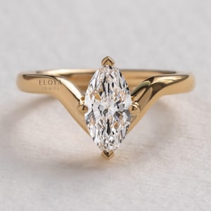 May include: A gold marquise-cut engagement ring. The ring features a large, clear, marquise-cut diamond set in a gold band. The band has a unique, curved design with small decorative accents. The brand name "ELOYA JEWEL" is visible on the ring.