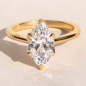 May include: A gold ring with a pear-shaped diamond. The diamond is set with four prongs and is the focal point of the ring. The band is a smooth, polished gold. The ring is set against a neutral background.