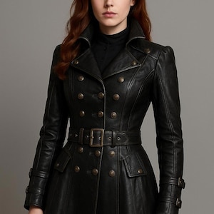 Op de afbeelding: Een zwarte leren jas met een dubbele rij knopen, met meerdere bronskleurige knopen en een bijpassende riem. De jas heeft een hoge kraag, epauletten en een uitlopende rok, waardoor een klassiek, getailleerd silhouet ontstaat.
