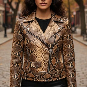 Peut inclure: Veste en cuir marron et beige à motif peau de serpent, avec un haut noir en dessous. La veste de style motard classique a un col cranté, une fermeture éclair asymétrique et une ceinture à la taille. La personne est dans une rue pavée.