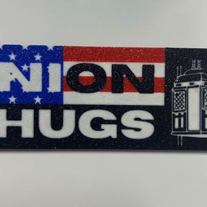 May include: A rectangular sticker with the words "UNION THUGS" in white block letters. The left side features a blue background with white stars, the middle has red and white stripes, and the right side has a black background with a white illustration of a cable car.