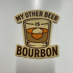 May include: A tan-colored magnet with the text "MY OTHER BEER IS BOURBON" in brown lettering. The magnet features a graphic of a whiskey glass with an ice cube.