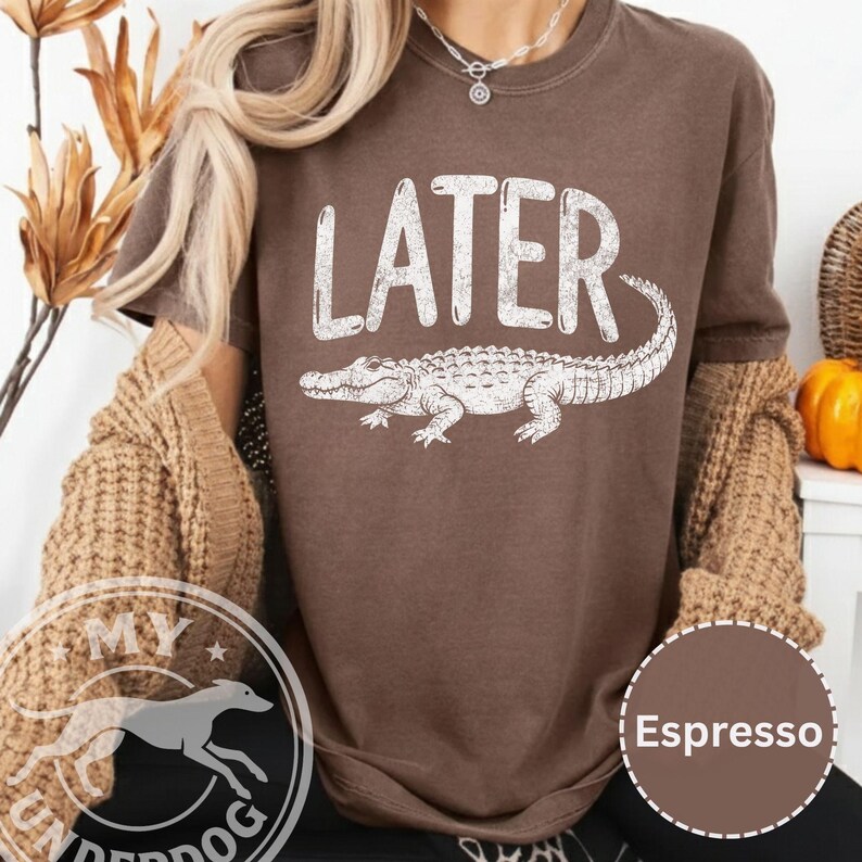 Pode incluir: Camiseta marrom com a palavra "LATER" em branco acima de uma ilustra&ccedil;&atilde;o de um jacar&eacute; branco. A camiseta &eacute; de estilo casual e a cor &eacute; descrita como "Espresso".