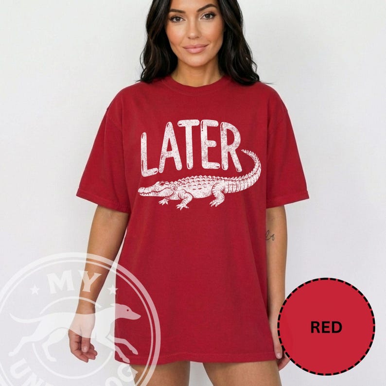 Pode incluir: T-shirt vermelha com a palavra "LATER" em branco, sobre uma ilustra&ccedil;&atilde;o de um jacar&eacute; branco. A t-shirt &eacute; de cor vermelha lisa e tem mangas curtas.