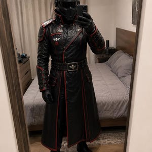 May include: A black leather-style trench coat with red piping, a matching belt with a skull emblem, and shoulder armor. The outfit includes a black and red full-face helmet with a skull logo, black gloves, and black boots, creating a uniform look.