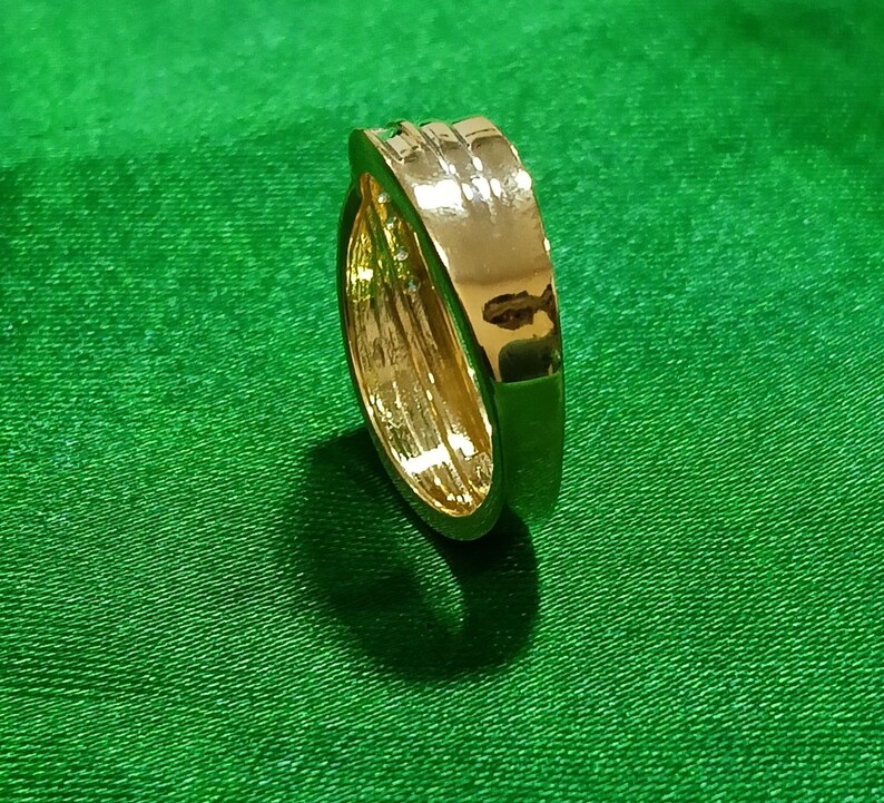 May include: A polished gold-tone metal ring featuring a smooth, wide band with a slightly raised, rounded center section. The surface of the ring is highly reflective, showing light highlights and a metallic finish throughout the entire piece.