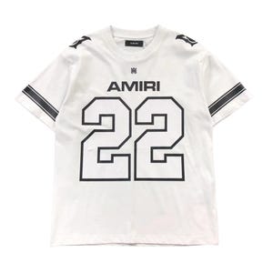 Puede incluir: Una camiseta blanca de manga corta con el texto AMIRI y el número 22 en grandes letras negras en la parte delantera. La prenda incluye rayas negras en las mangas, un pequeño logotipo en el cuello y detalles gráficos negros en los hombros.