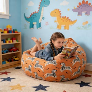 May include: An orange beanbag chair with a zebra pattern. A young person is lying on the beanbag, reading a book. The room has a blue wall with dinosaur decals and a wooden bookshelf with toys. A star-patterned rug is on the floor.