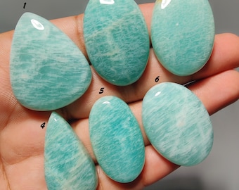 May include: Six polished amazonite cabochons in shades of light blue-green with white veining, labeled with numbers one through six. The stones feature smooth, rounded surfaces and varied shapes, including teardrop and oval forms, displaying natural patterns.
