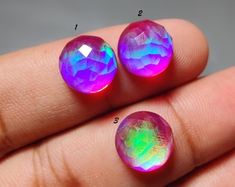 Puede incluir: Tres piedras preciosas redondas y facetadas etiquetadas 1, 2 y 3. Las piedras exhiben un juego de colores vibrante con tonos cambiantes de magenta, rosa y azul eléctrico. Cada gema presenta una superficie pulida y multifacetada.
