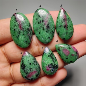 Pode incluir: Seis pedras preciosas de zoisite polida com inclusões de rubi, numeradas de um a seis. As pedras apresentam uma base verde vibrante com depósitos minerais pretos salpicados e manchas distintas de rubi vermelho rosado profundo.