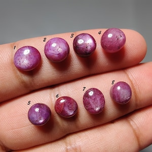 Pode incluir: Oito pedras preciosas cabochão redondas, polidas, de cor rosa profundo a magenta, dispostas em duas filas. Cada pedra é numerada de um a oito com tinta preta. As pedras exibem inclusões naturais e níveis variados de translucidez.