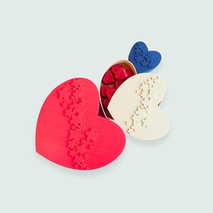 May include: Heart-shaped boxes in red, white, and blue, each adorned with floral patterns. One box is open, revealing red heart-shaped candies. A charming presentation for Valentine's Day or a special occasion.