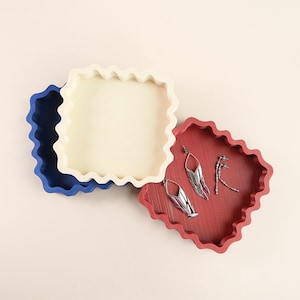 Peut inclure: Ensemble de trois mugs en céramique avec une finition mate et mouchetée. Les tasses sont de couleur crème, gris clair et gris foncé. Chaque mug a un design simple et minimaliste.