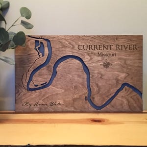 Puede incluir: Arte de pared de madera que presenta un mapa detallado del río Current en Missouri, con una incrustación de río de epoxi azul. El texto "Current River Missouri" y "My Home Water" están grabados en la madera, junto con una rosa de los vientos.