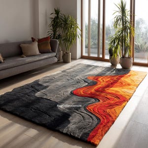 May include: A rectangular area rug with a unique design. The rug features a color gradient from black to gray, with a vibrant orange and red wave pattern. The rug is placed on a wooden floor in a living room setting.