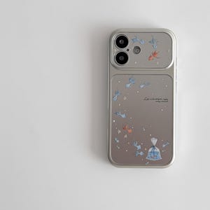 May include: Silver phone case with a design of blue and orange fish, stars, and a bag of fish. The text "Life is beautiful; enjoy every moment" is printed on the case.