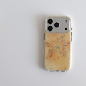 Könnte beinhalten: Transparente Handyhülle mit einem gelb-goldenen Feuerwerksdesign. Die Hülle hat einen glitzernden silbernen Rand um die Kamera und den Text "Twinkle Glow".