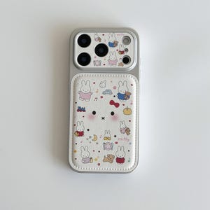 May include: A phone case with a white and gray design featuring a cartoon bunny character. The case has a white leather-like panel with the bunny and other small illustrations. The top portion is gray with camera cutouts.