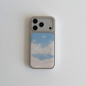 Könnte beinhalten: Silberne Handyhülle mit hellblauem Hintergrund mit Wolken- und Pegasus-Design. Die Hülle hat einen silbernen Rahmen und einen rechteckigen Einsatz mit dem Kunstwerk. Das Design umfasst zwei Pegasus-Figuren.