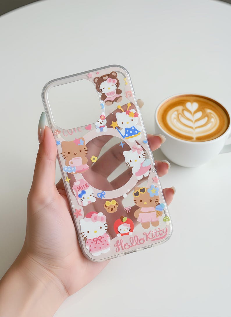 May include: Clear phone case featuring Hello Kitty and other cartoon characters in various outfits. The case has a pink border and the words "Hello Kitty" are printed on the bottom. A cup of coffee with latte art is in the background.