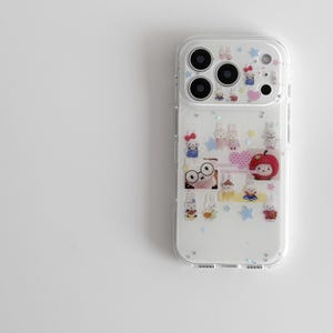 以下が含まれることがあります： 漫画のウサギ、星、ハートで飾られた透明な携帯電話ケース。ケースは透明な縁と白い背景を持っています。デザインには赤いリンゴとピンクのハートが含まれています。ケースはスマートフォン用に設計されています。